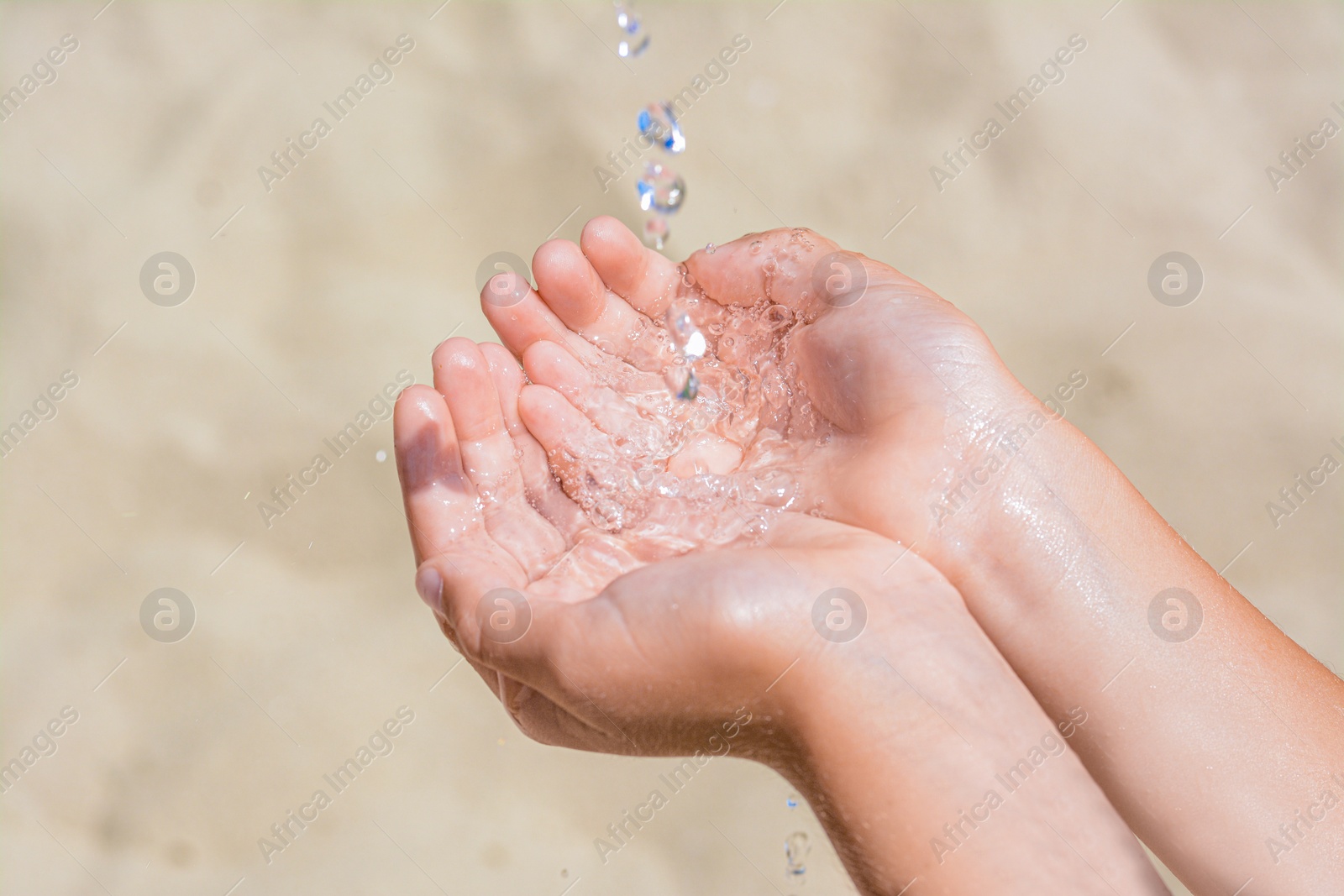 Photo of Pouring water into kid`s hands outdoors, closeup