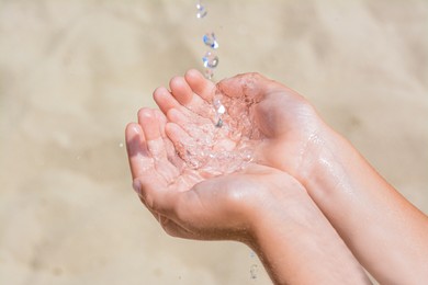 Pouring water into kid`s hands outdoors, closeup