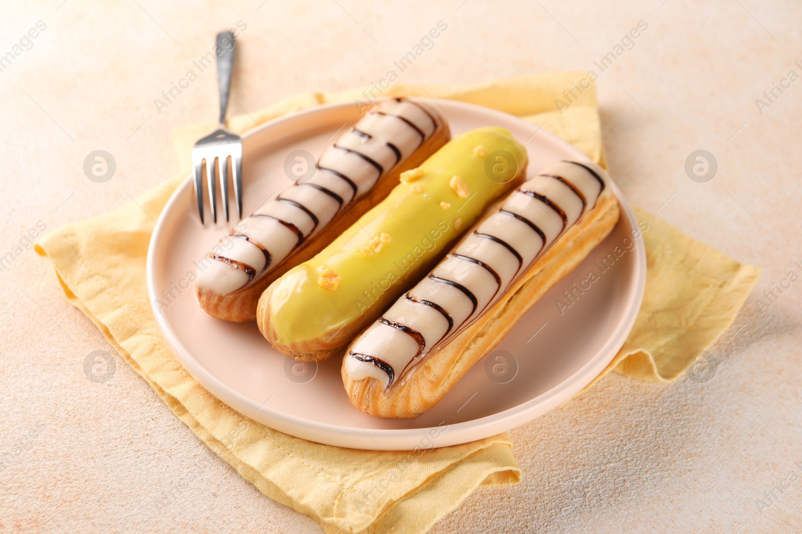 Photo of Different tasty glazed eclairs served on color textured table, closeup