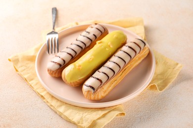 Different tasty glazed eclairs served on color textured table, closeup