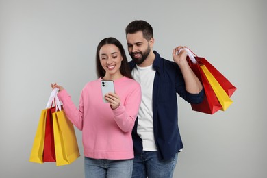 Photo of Happy couple with shopping bags and smartphone on grey background