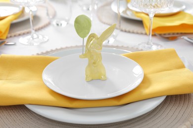 Photo of Festive table setting with cutlery, plate and bunny figure, closeup. Easter celebration