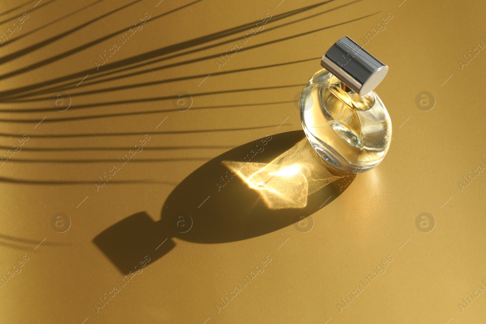 Photo of Luxury women's perfume. Sunlit glass bottle on golden background, space for text