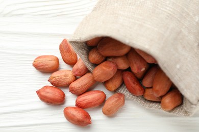 Photo of Fresh peanuts in sack on white wooden table, above view