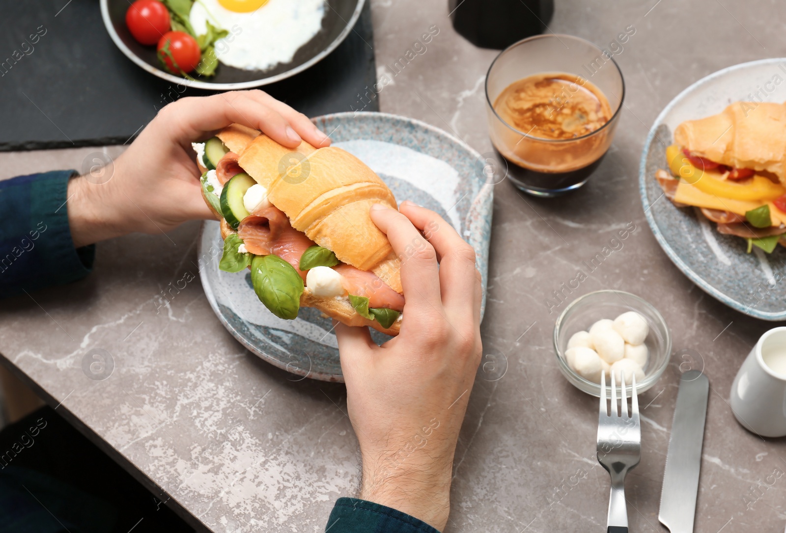 Photo of Man holding tasty croissant sandwich over plate at table