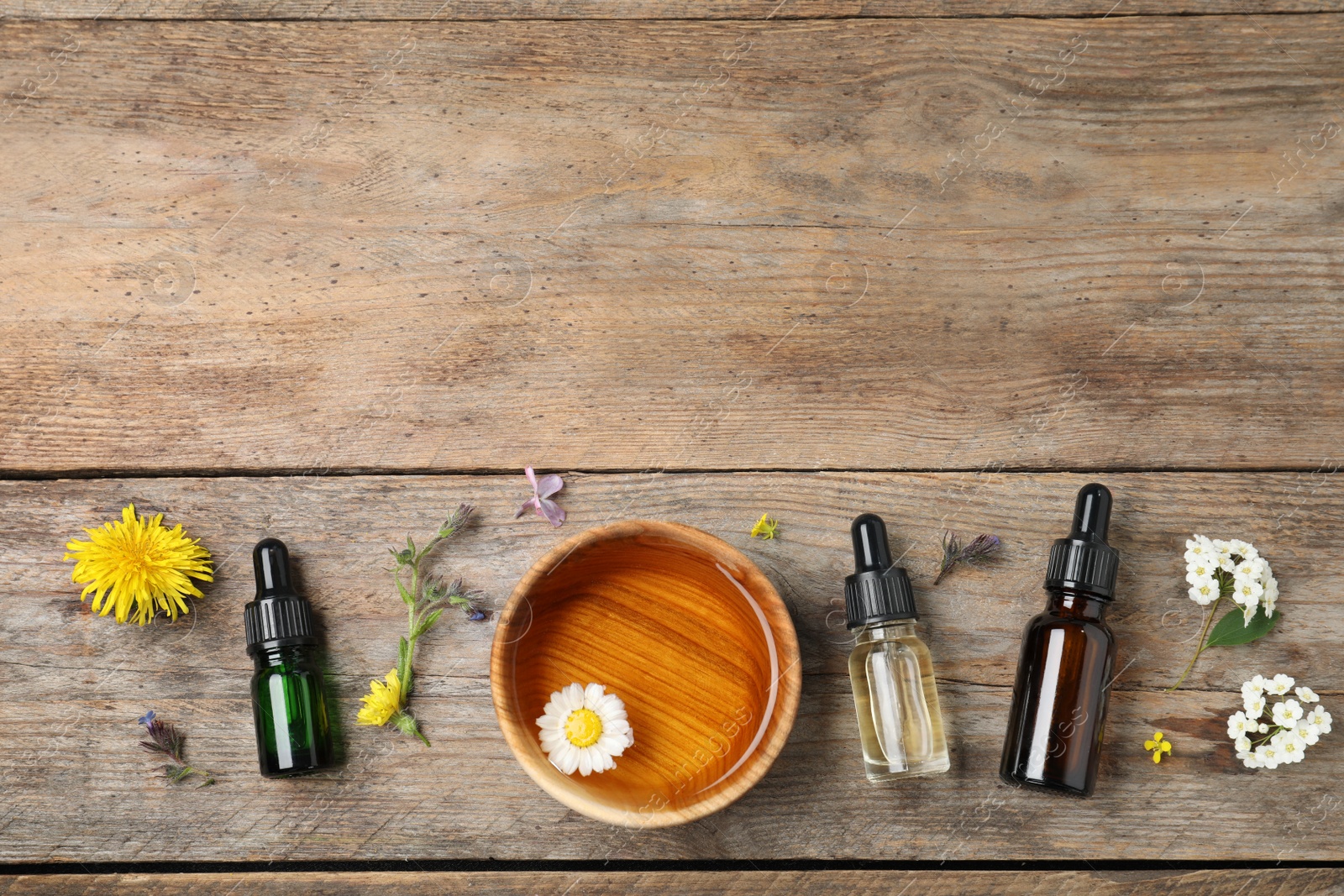 Photo of Flat lay composition with essential oils, bowl and flowers on wooden table, space for text