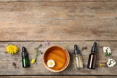 Flat lay composition with essential oils, bowl and flowers on wooden table, space for text