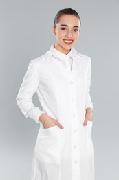 Photo of Happy young woman in lab coat on light grey background