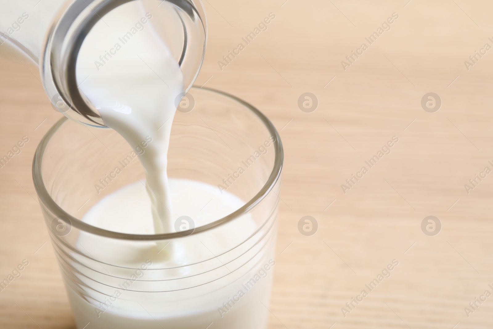 Photo of Pouring milk into glass on table, closeup. Space for text