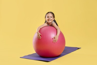 Photo of Cute little girl with fit ball on yellow background