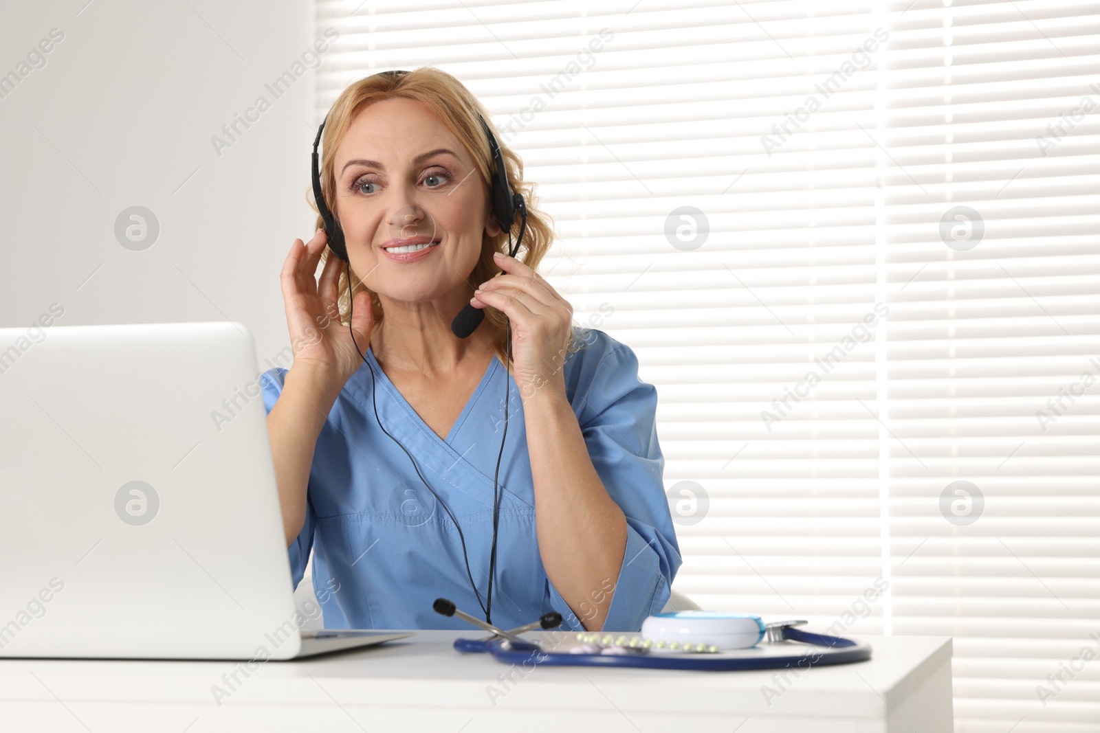 Photo of Doctor with laptop and headphones consulting patient in clinic. Online medicine concept