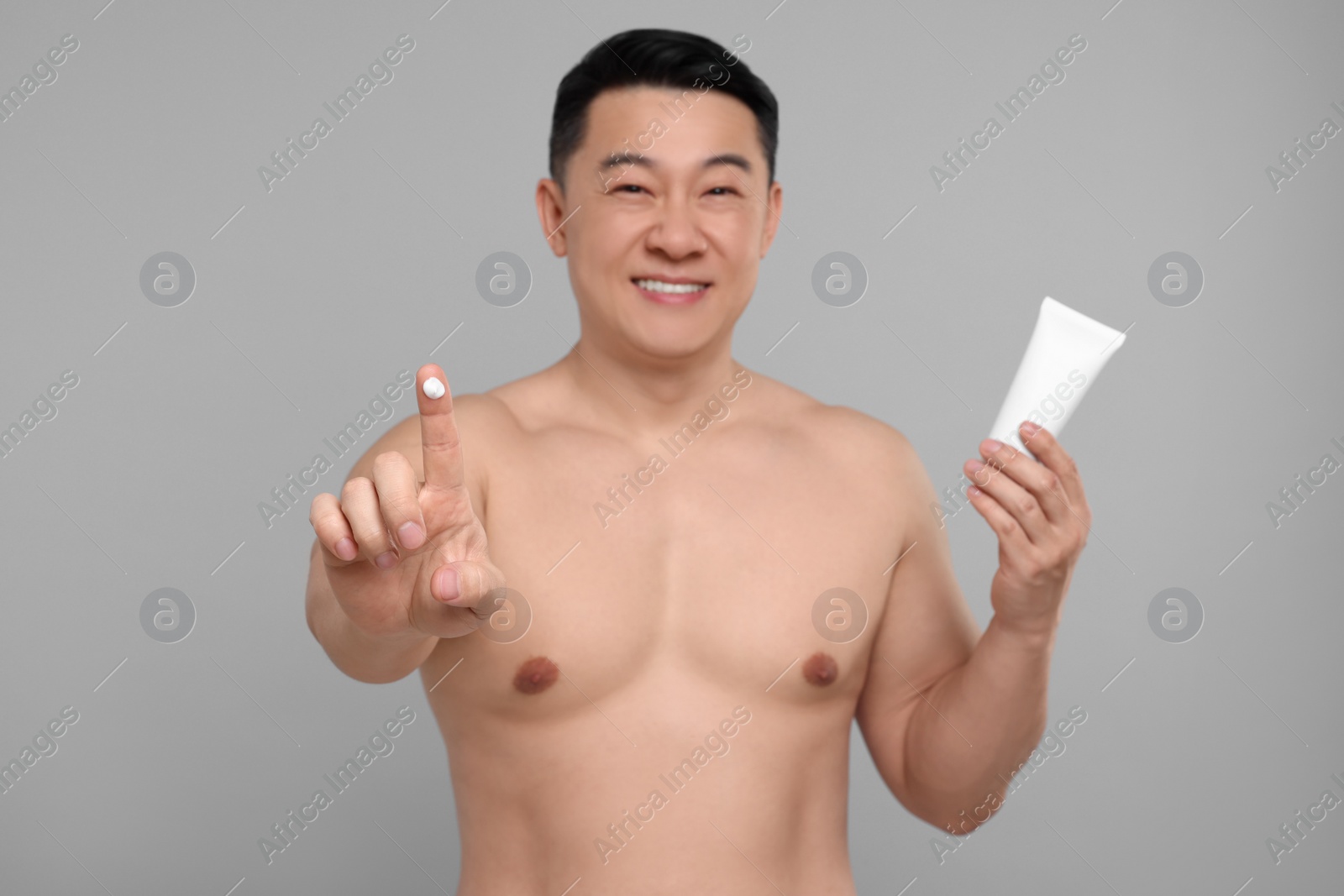 Photo of Handsome man with tube of body cream on light grey background, selective focus