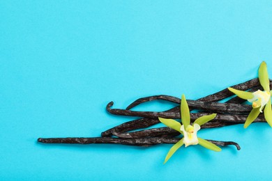 Photo of Vanilla pods and beautiful flowers on light blue background, top view. Space for text