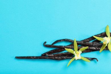 Vanilla pods and beautiful flowers on light blue background, top view. Space for text