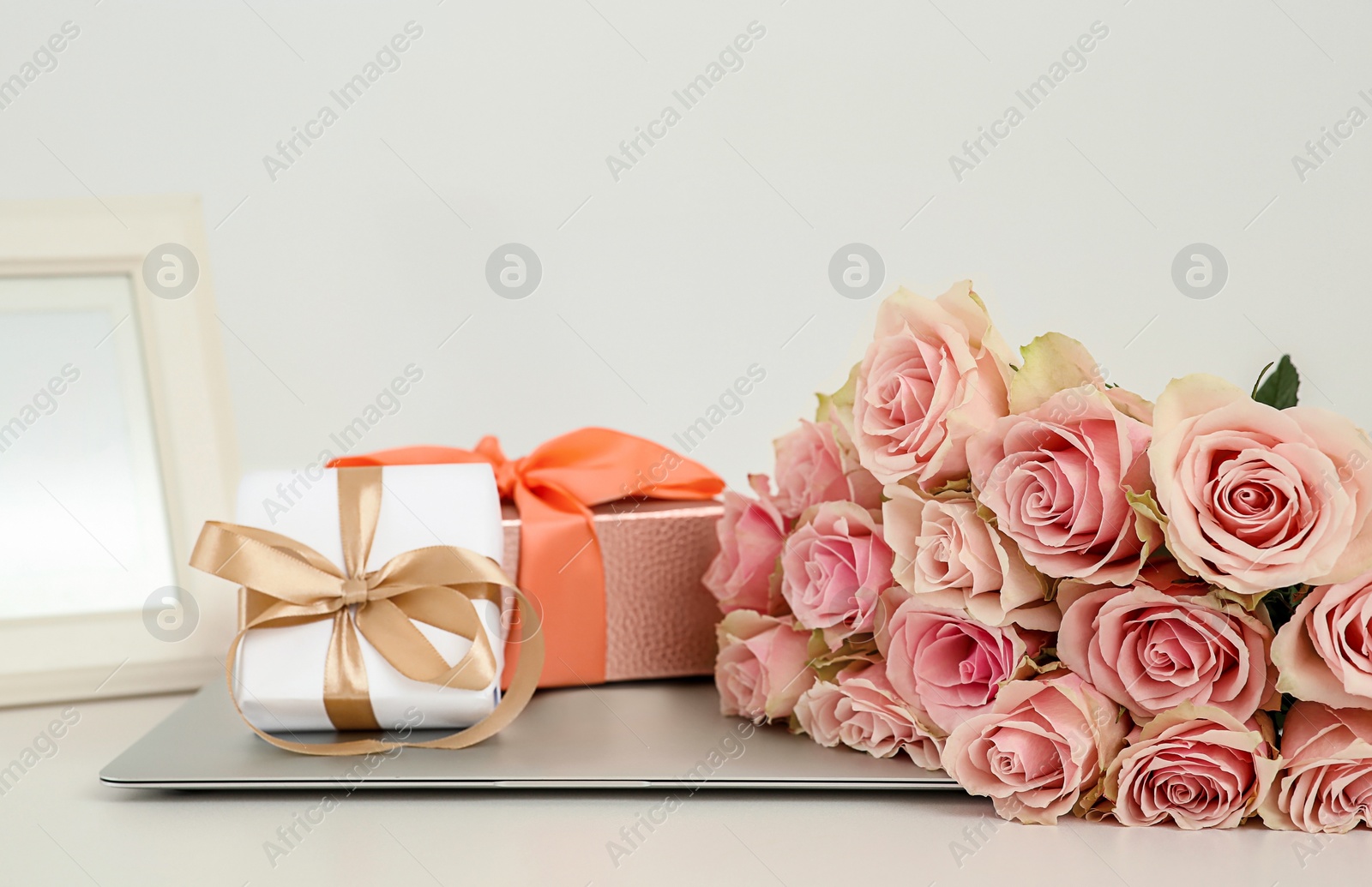 Photo of Beautiful bouquet of roses, gifts and laptop on white table. Happy birthday greetings
