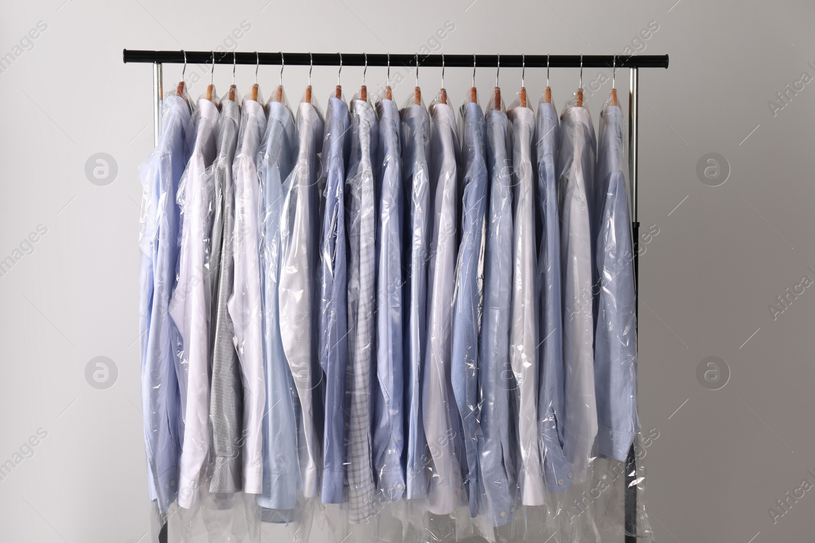 Photo of Hangers with shirts in dry cleaning plastic bags on rack against light background