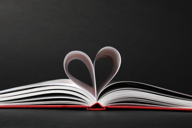 Photo of Open book with pages folded in heart on black background