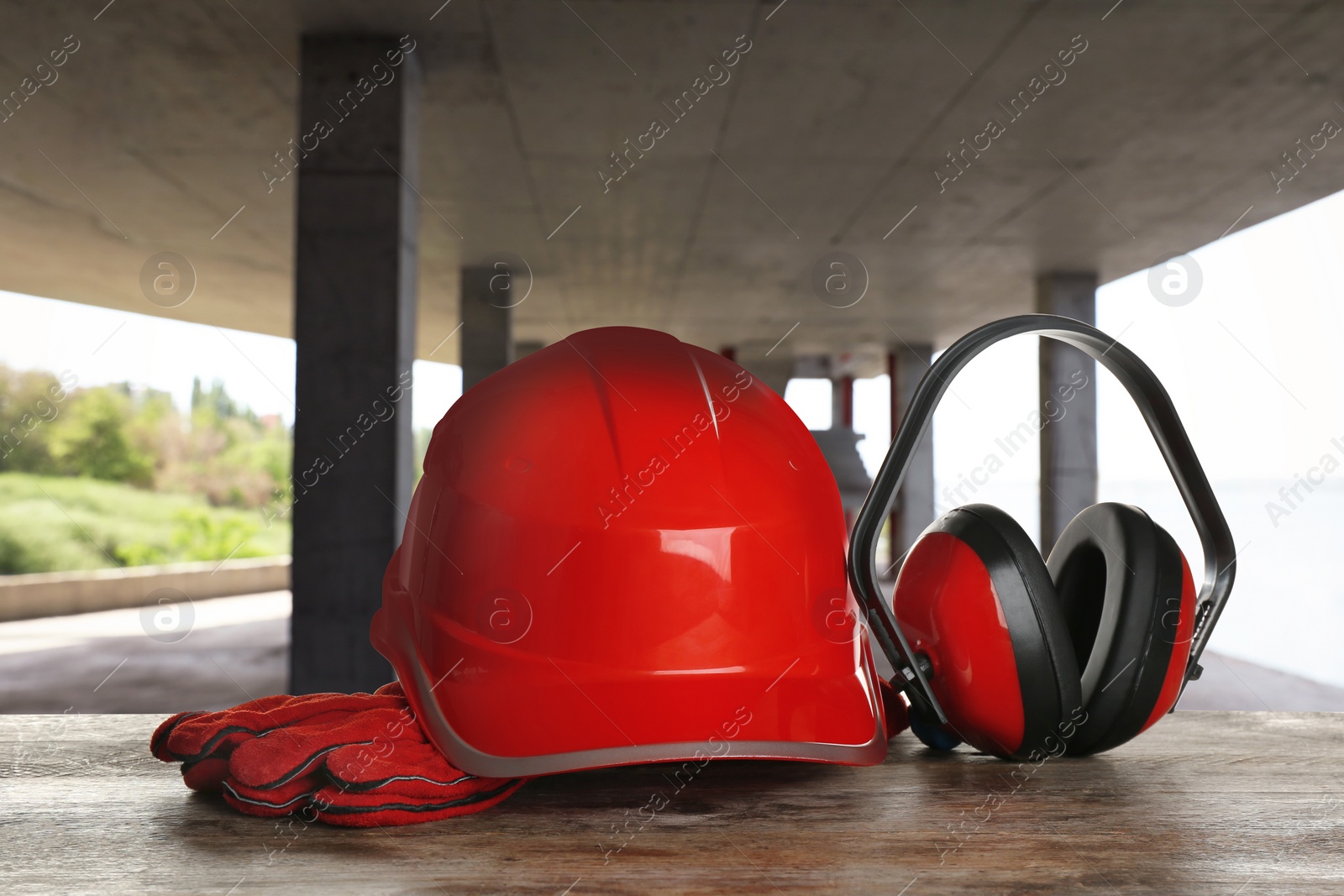 Image of Safety equipment. Hard hat, gloves and protective headphones on wooden surface inside of unfinished building