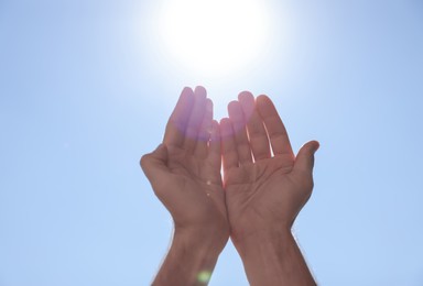 Man reaching hands to blue sky outdoors on sunny day, closeup