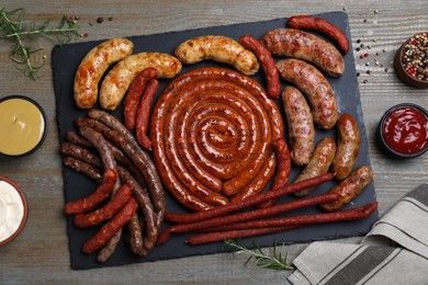 Photo of Different delicious sausages and sauces on wooden table, flat lay. Assortment of beer snacks