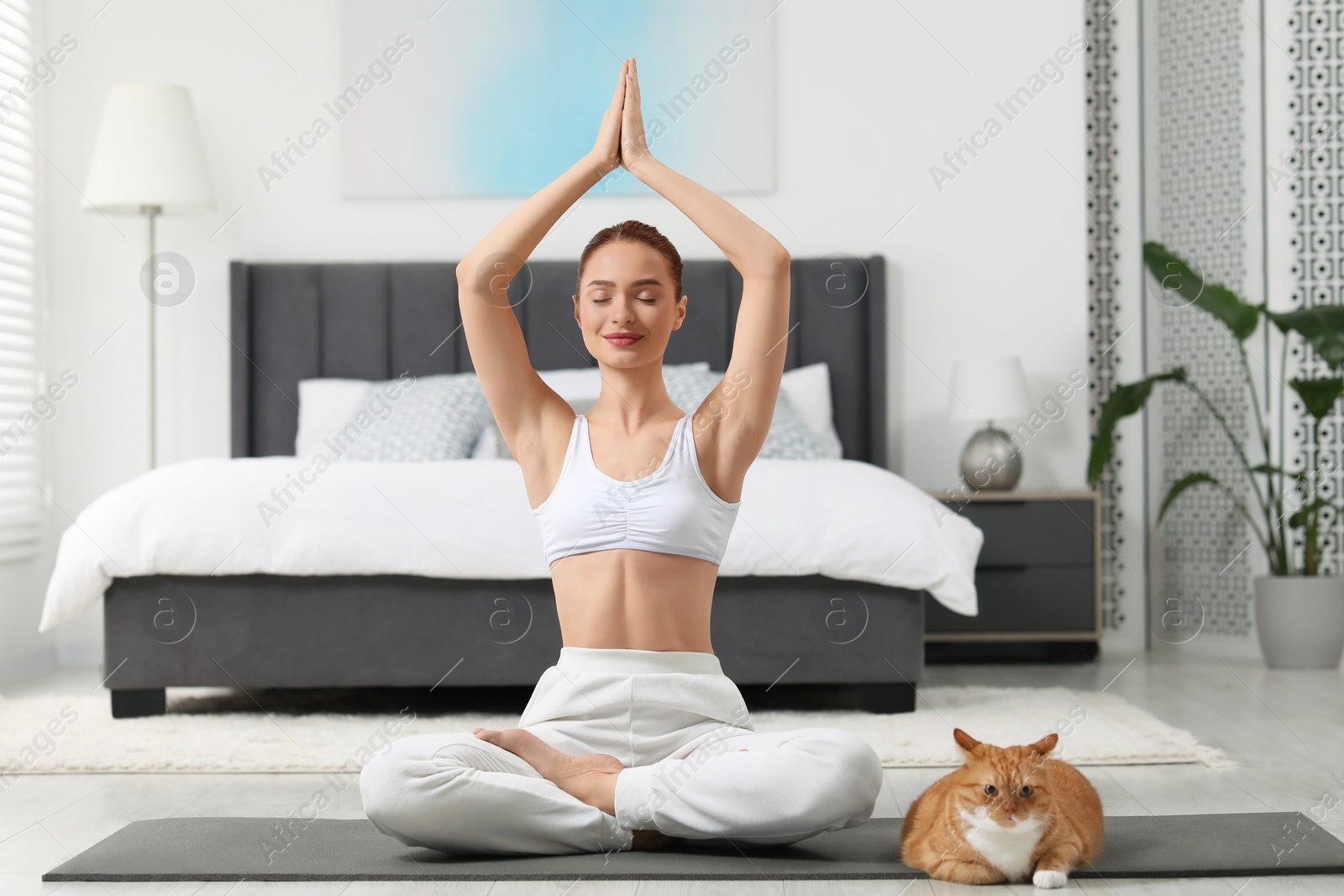 Photo of Beautiful woman with cute red cat practicing yoga on mat at home