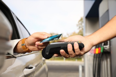 Photo of Man sitting in car and paying with credit card at gas station, closeup