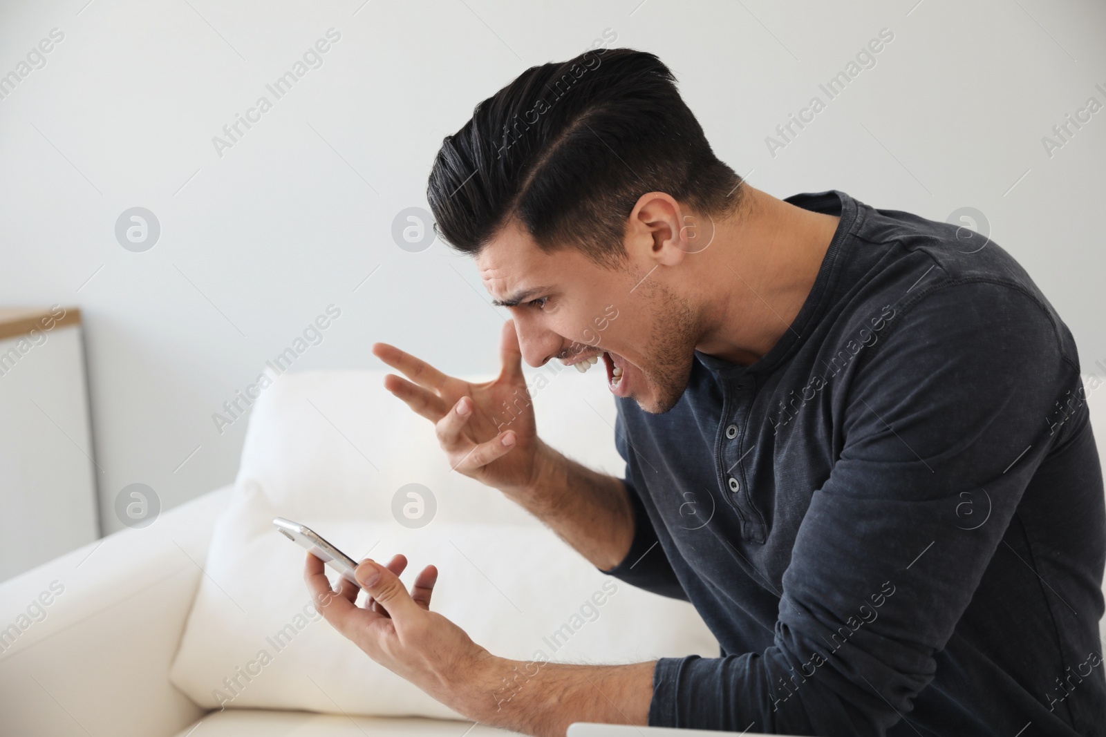 Photo of Emotional man shouting at smartphone in room