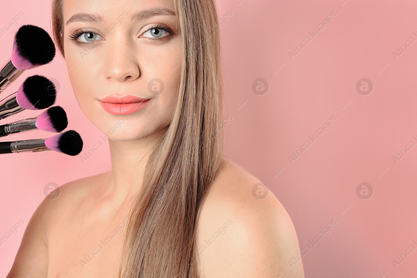 Photo of Portrait of beautiful young woman with makeup brushes on color background. Space for text