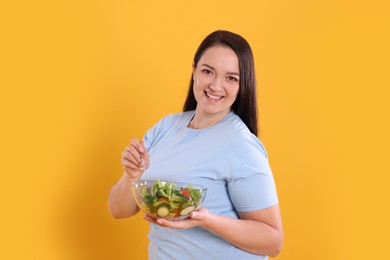 Photo of Beautiful overweight woman eating salad on yellow background. Healthy diet