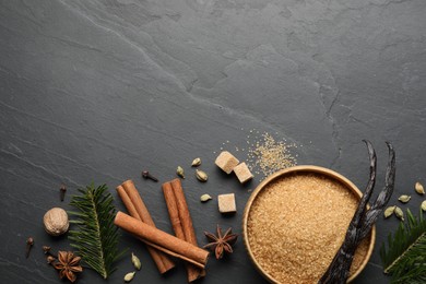 Photo of Different aromatic spices and fir branches on dark textured table, flat lay. Space for text