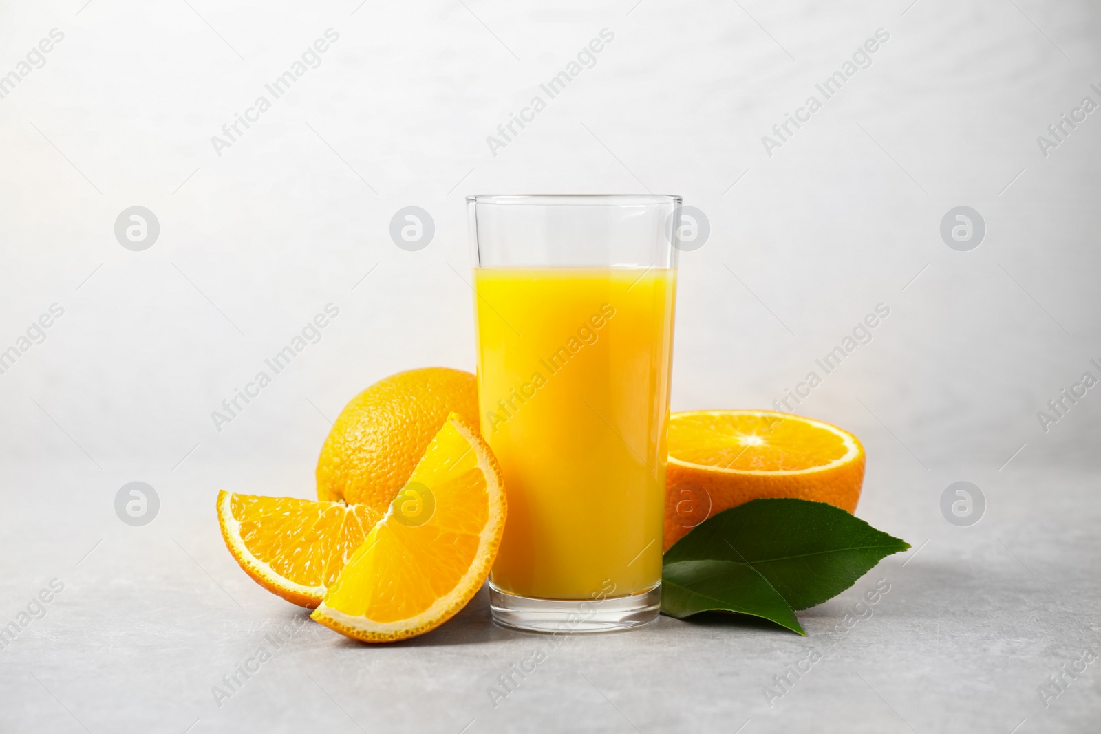 Photo of Tasty orange juice, fresh fruits and green leaves on light table