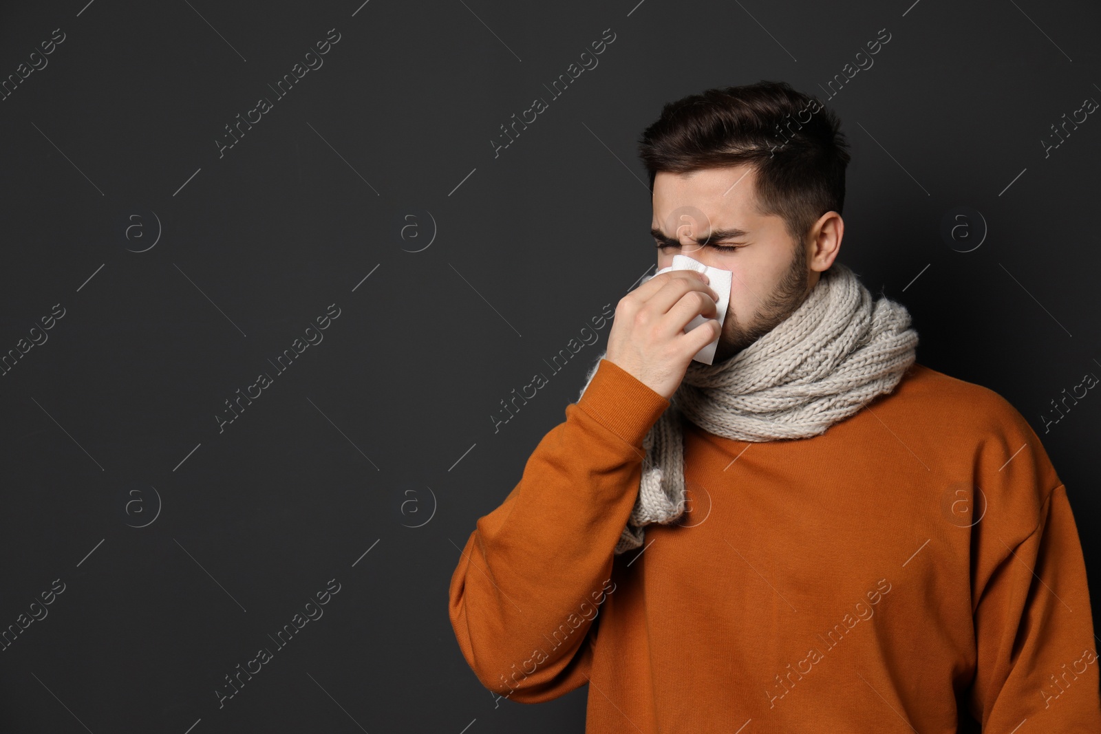Photo of Handsome young man blowing nose against dark background. Space for text