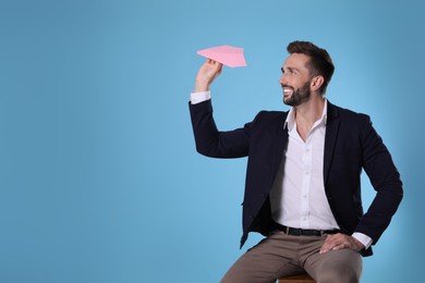 Photo of Handsome businessman playing with paper plane on light blue background. Space for text