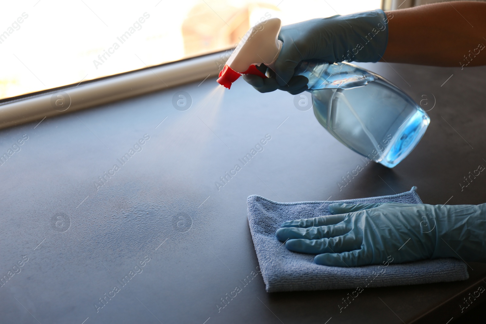 Photo of Woman in gloves cleaning grey window sill with rag and detergent indoors, closeup