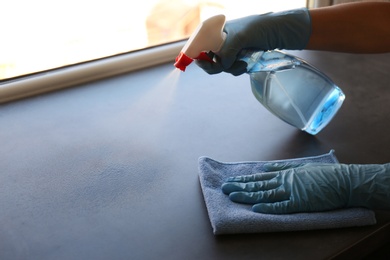 Woman in gloves cleaning grey window sill with rag and detergent indoors, closeup