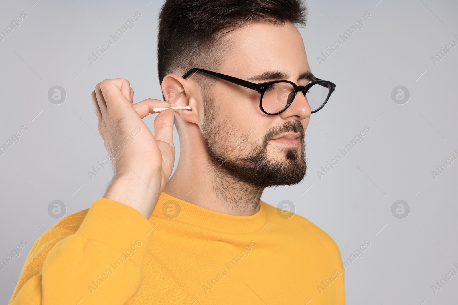 Photo of Young man cleaning ear with cotton swab on light grey background
