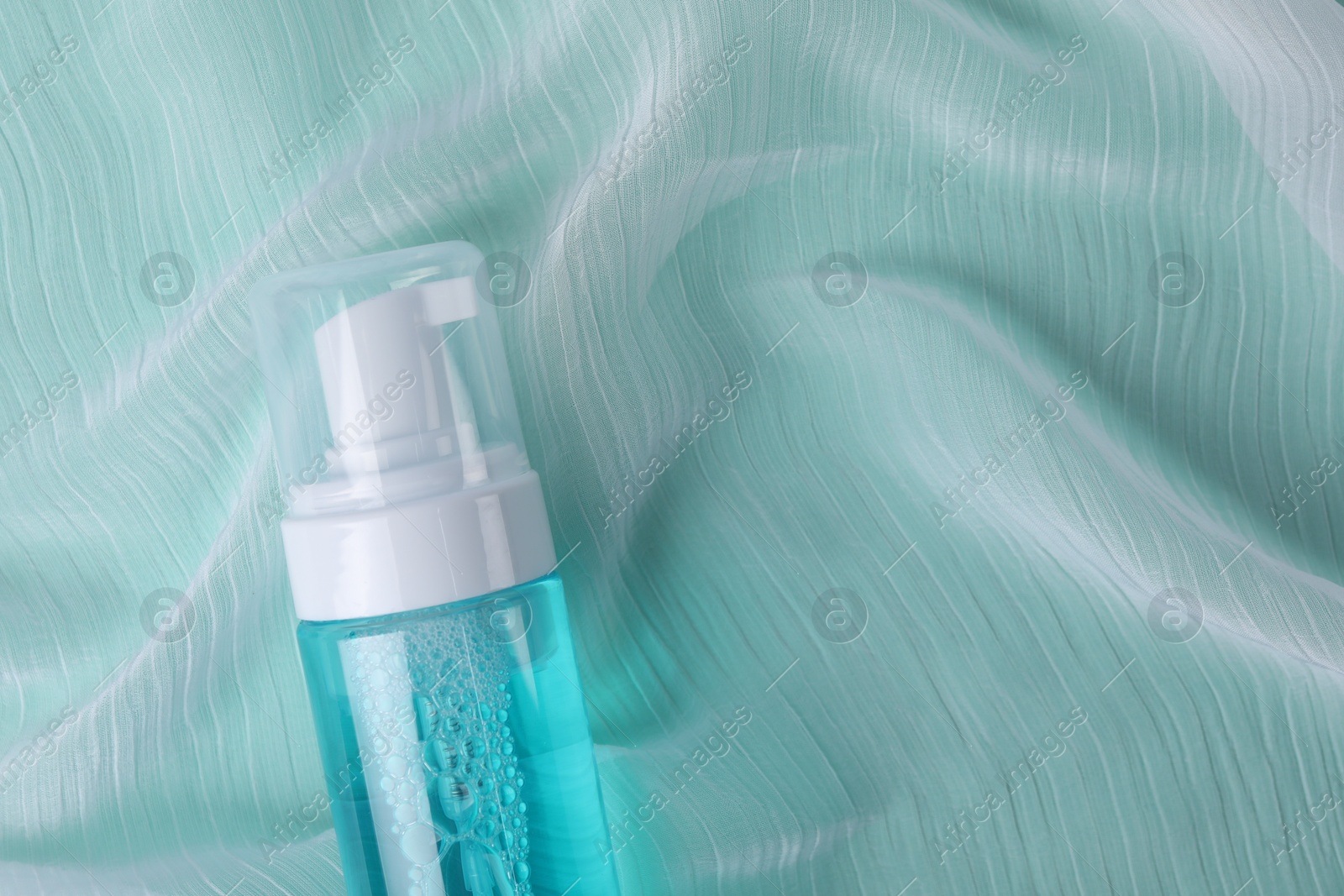 Photo of Bottle of face cleansing product on turquoise fabric, top view. Space for text