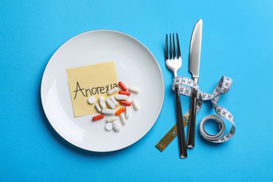 Photo of Flat lay composition with word Anorexia, table setting and pills on light blue background