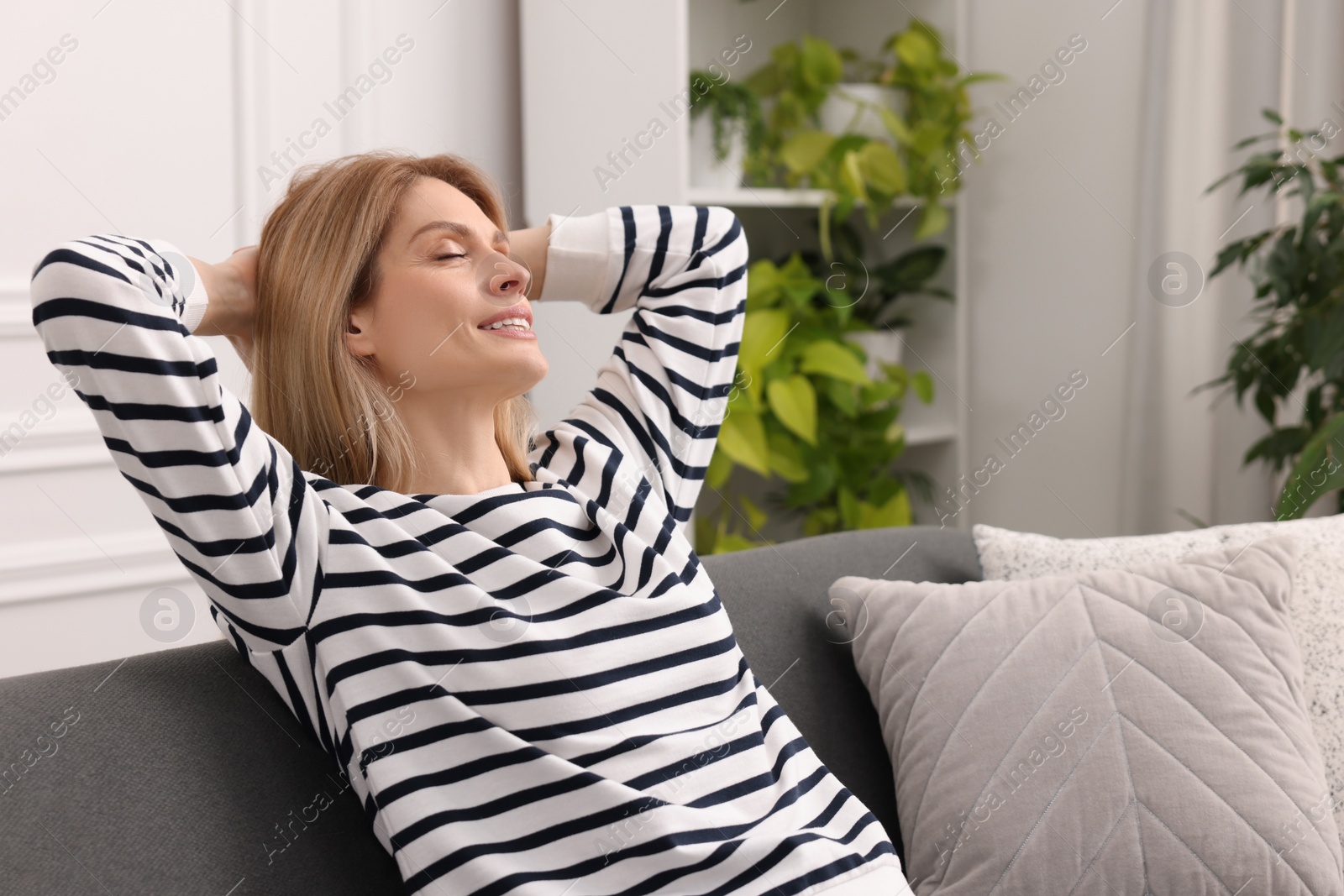 Photo of Woman relaxing on sofa in room with green houseplants