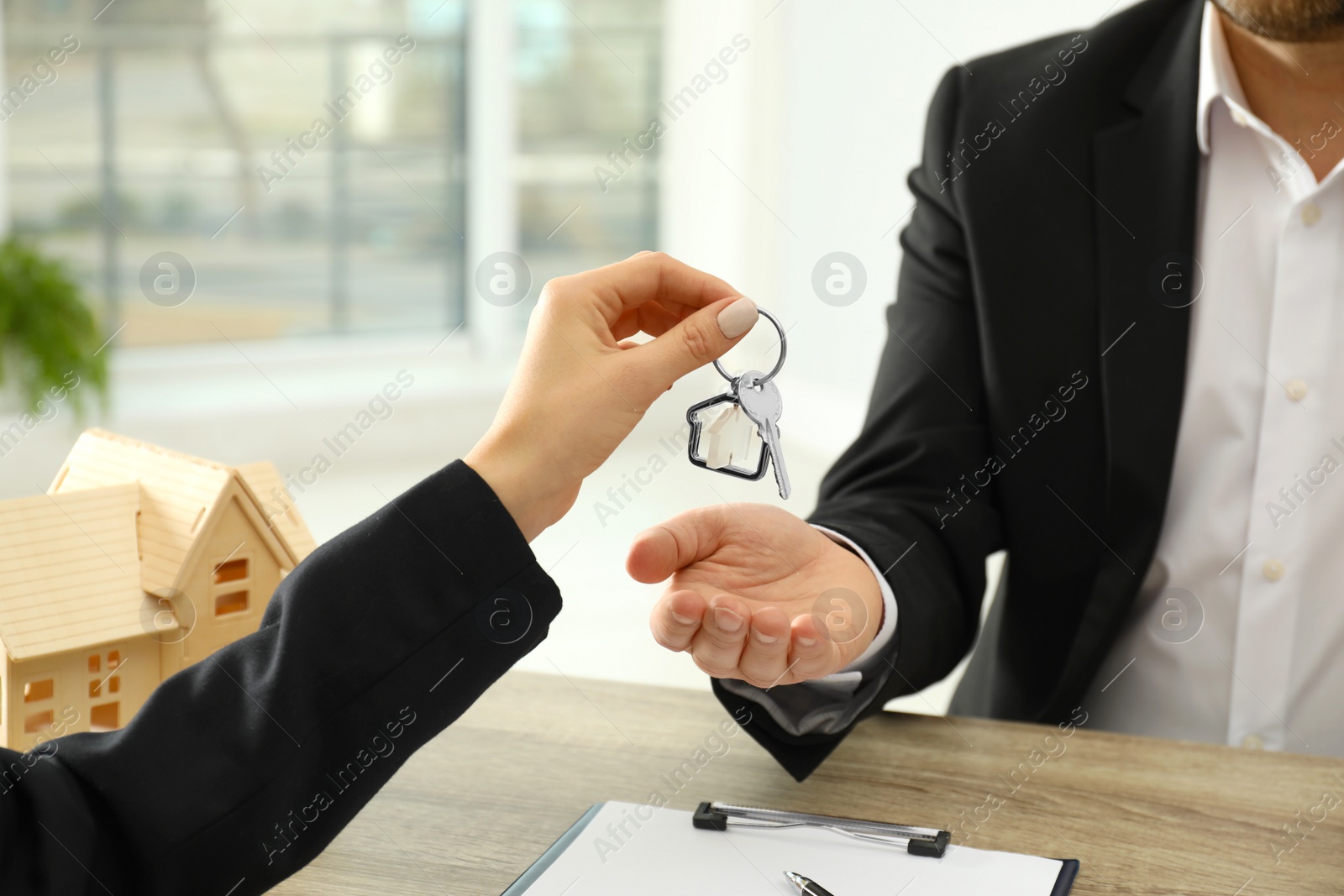 Photo of Real estate agent giving key to client at table in office, closeup