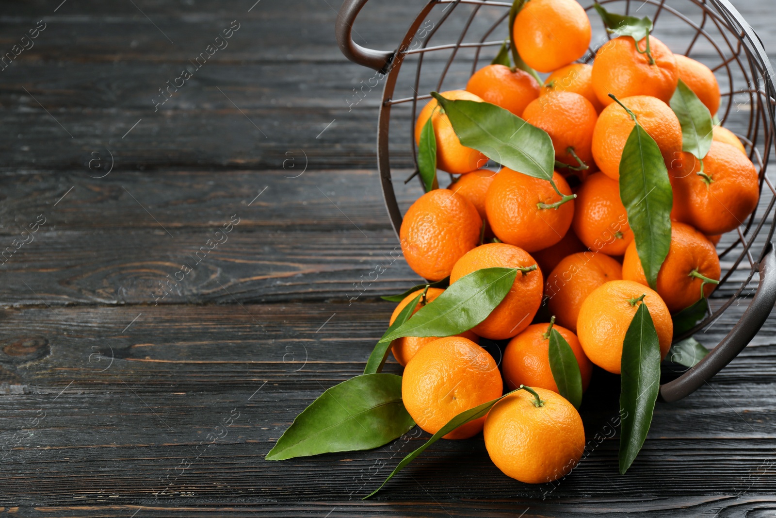 Photo of Fresh tangerines with green leaves on black wooden table, closeup. Space for text