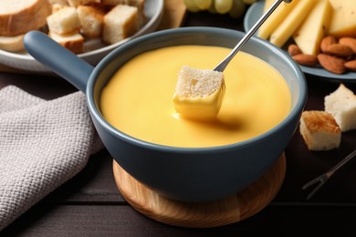 Photo of Dipping piece of bread into tasty cheese fondue at wooden table, closeup