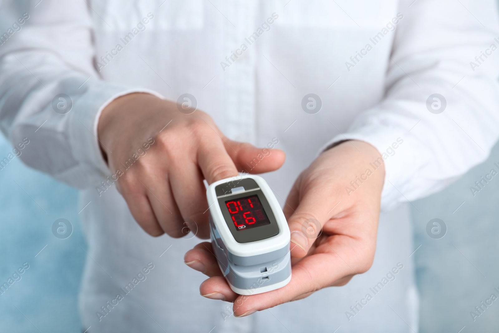 Photo of Woman using modern fingertip pulse oximeter on light background, closeup