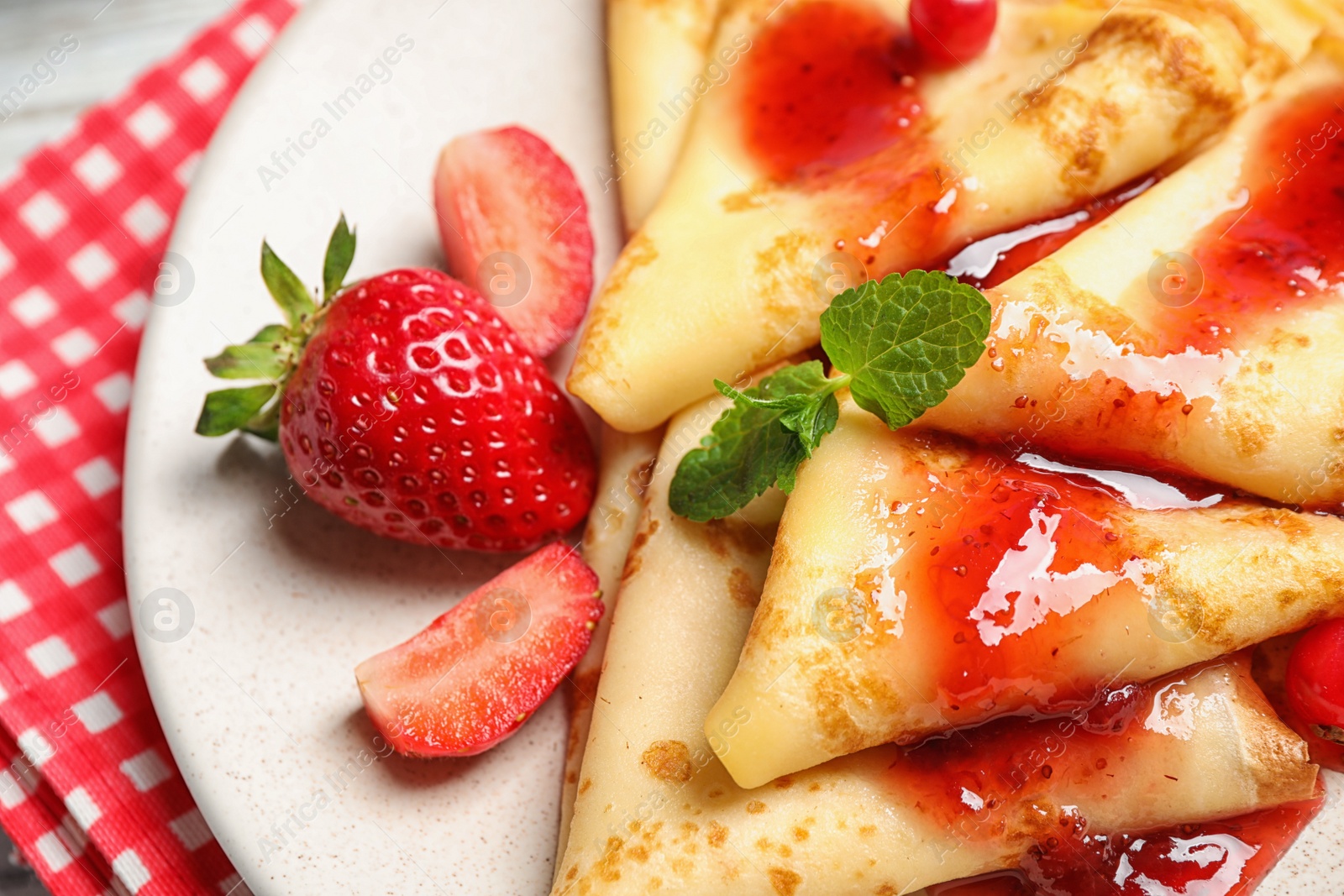 Photo of Delicious thin pancakes with strawberries and jam on plate, closeup