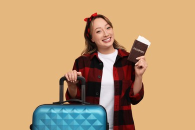 Happy young woman with passport, ticket and suitcase on beige background