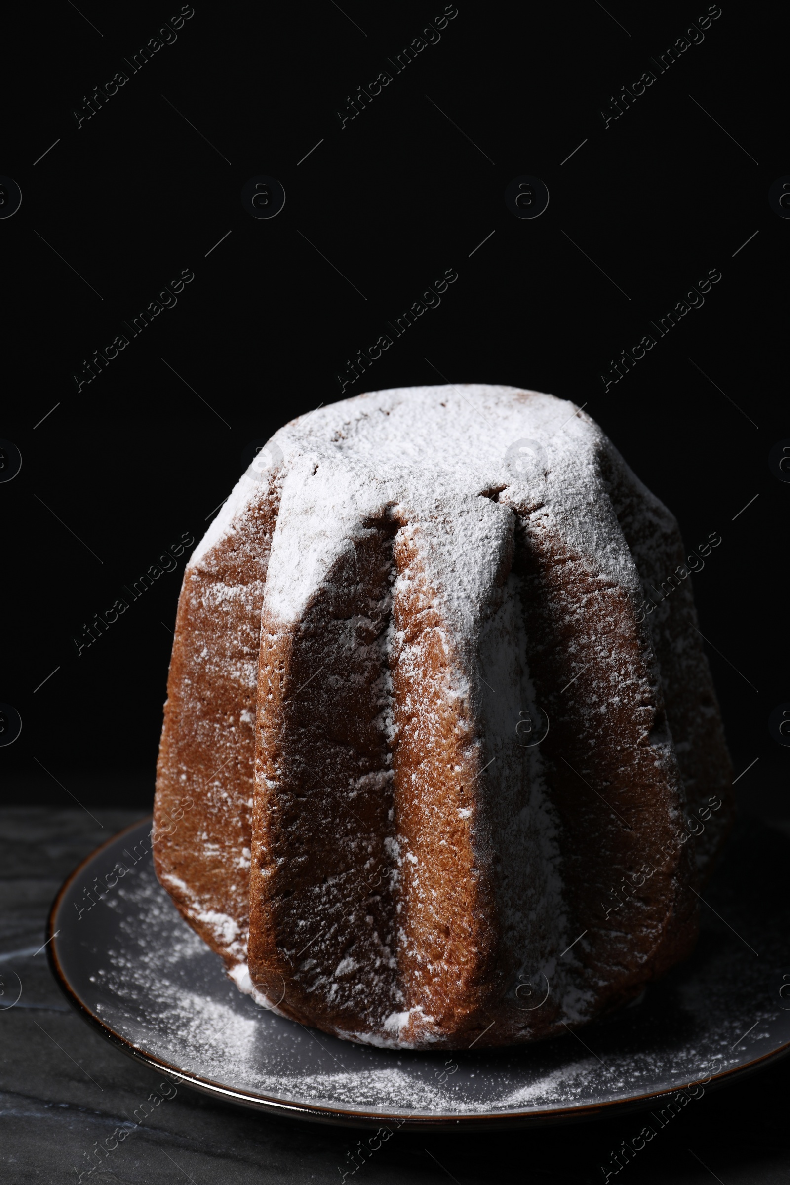 Photo of Delicious Pandoro cake decorated with powdered sugar on dark table. Traditional Italian pastry