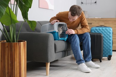 Photo of Travel with pet. Man closing carrier with cat on sofa at home