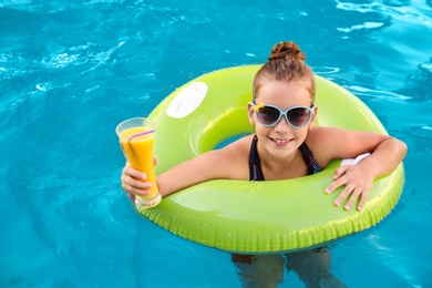 Photo of Happy little girl with inflatable ring and drink in swimming pool