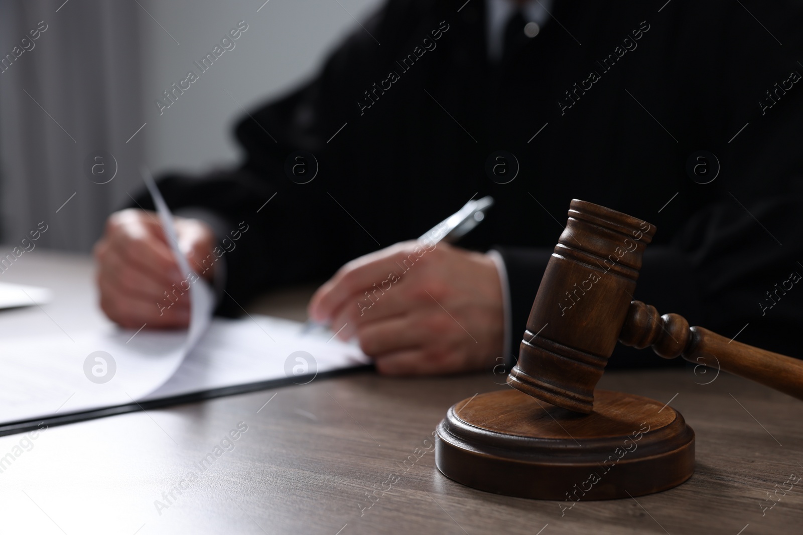 Photo of Judge with gavel writing in papers at wooden table, closeup