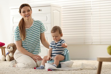 Photo of Mother training her child to sit on baby potty indoors. Space for text